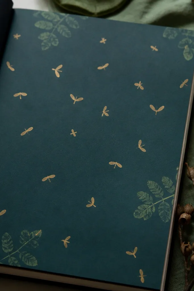 A dark teal journal page with scattered tiny seed pod shapes in gold ink, plus a few pale green leaf stamps near the edges.