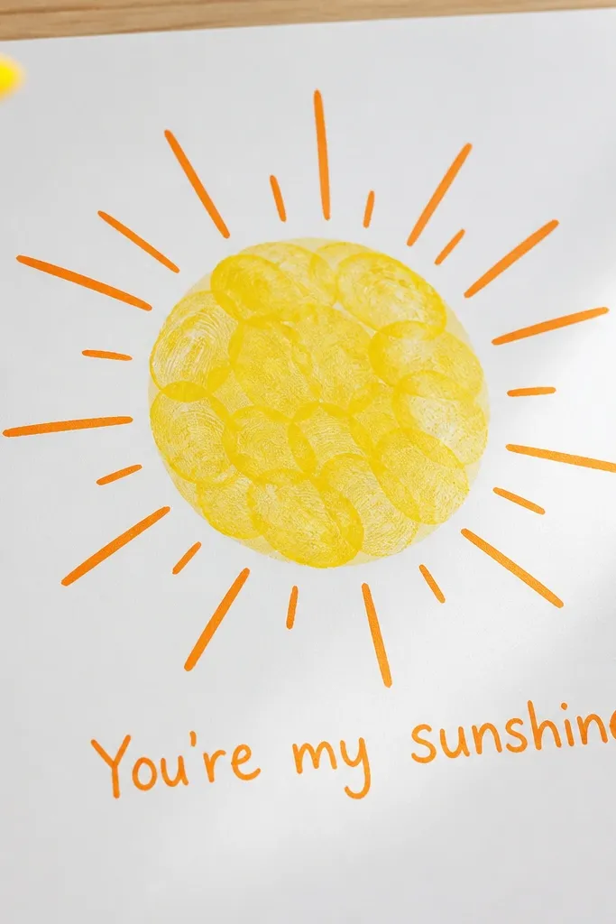 A bright yellow sun on white paper: the center is handprint/fingerprint textured, and the rays are drawn with orange marker. A short message reads “You’re my sunshine” near the bottom.
