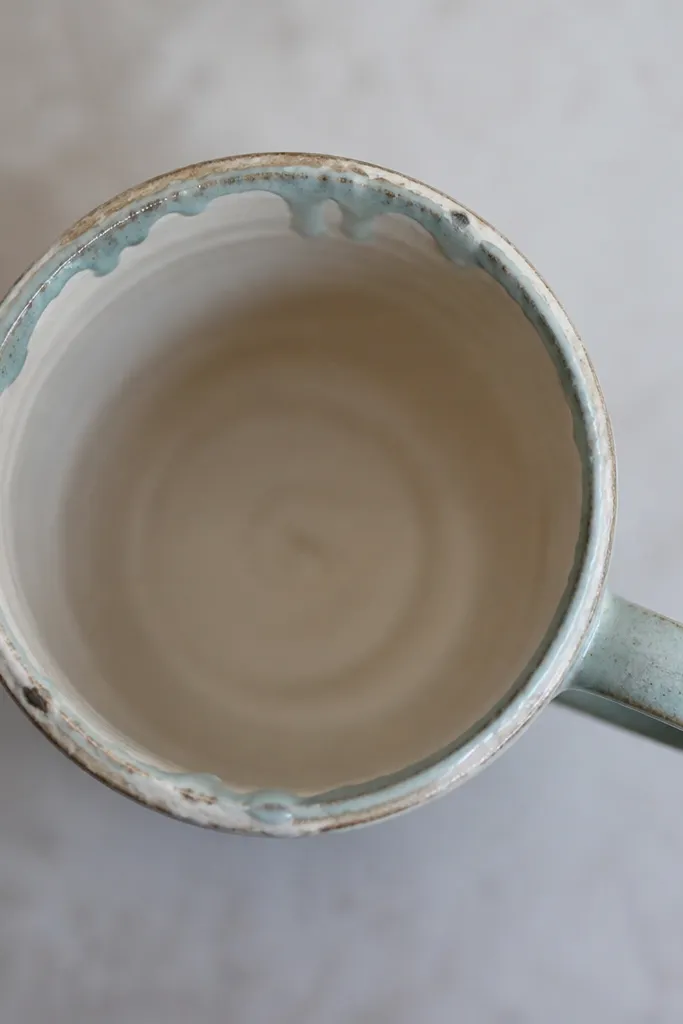 Top-down photo of a mug showing a messy glaze ring around the inner lip, with drips and a rough glaze edge where the rim was touched during glazing.