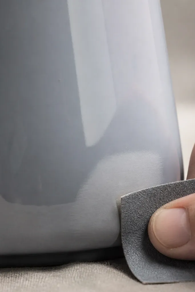 Close-up of sandpaper lightly scuffing the mug’s lower curve, with a small dust-free area and the rest of the mug still glossy.