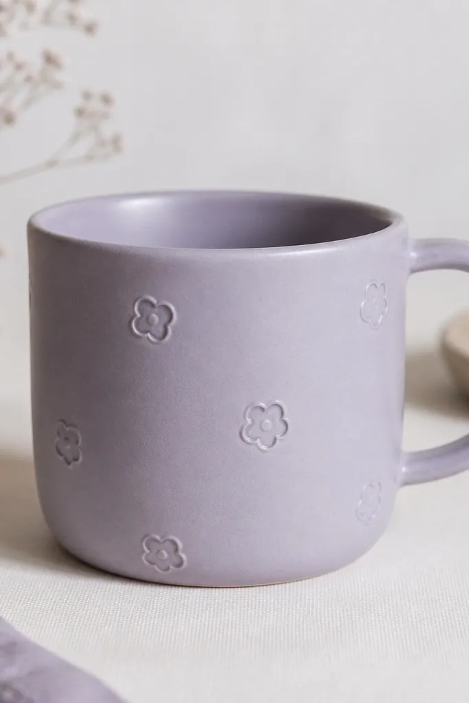 A mug with small, shallow raised flower outlines spaced around the side, with a soft lavender-toned clay body color.