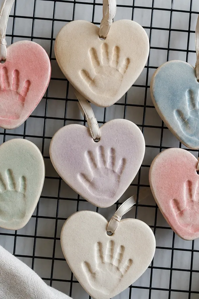 Salt dough heart ornaments with handprint details, baked and lightly painted, with a ribbon loop at the top, displayed on a cooling rack.