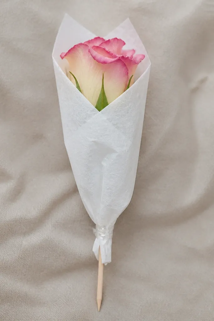 A skewer stem wrapped in a small tissue paper sleeve with the flower peeking out, secured with clear tape at the bottom twist.